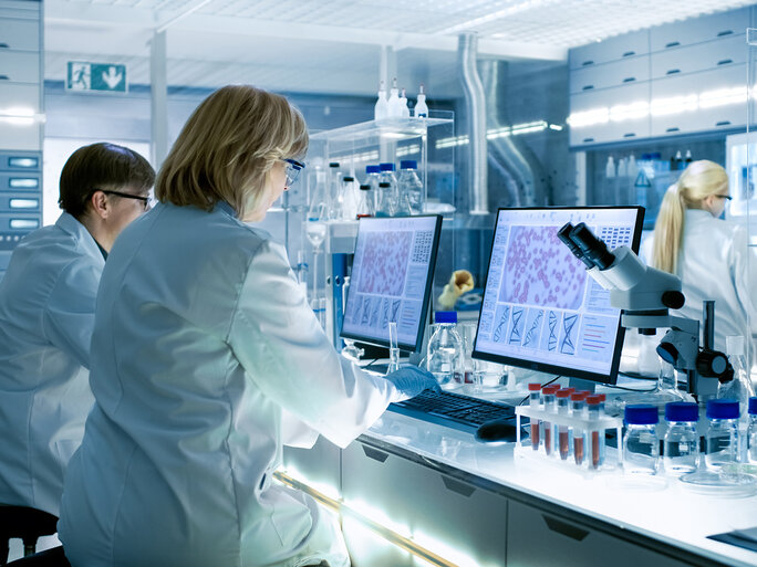 Scientists analyzing cell culture images and experimental data at a laboratory workstation with microscopes and digital imaging systems.